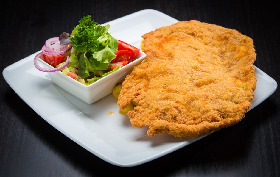 Golden crispy schnitzel served with a fresh vegetable salad, presented on a square plate.